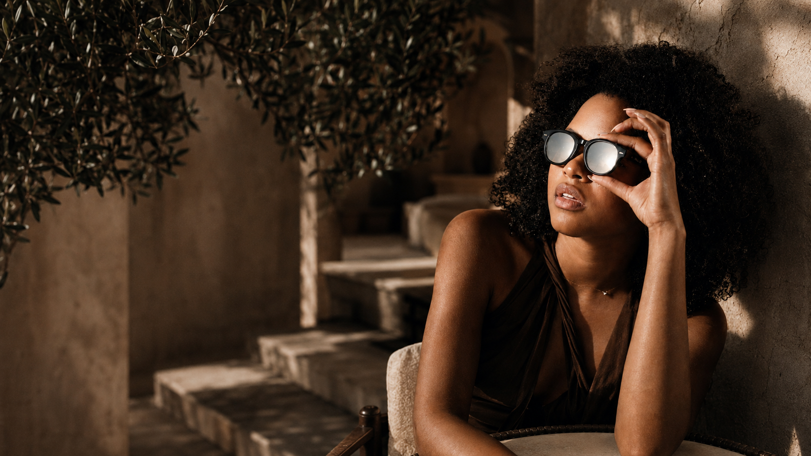A woman lifts the silver HALO eclipse overlay from her acetate frame to look up at the sun in a sunlit Mediterranean courtyard